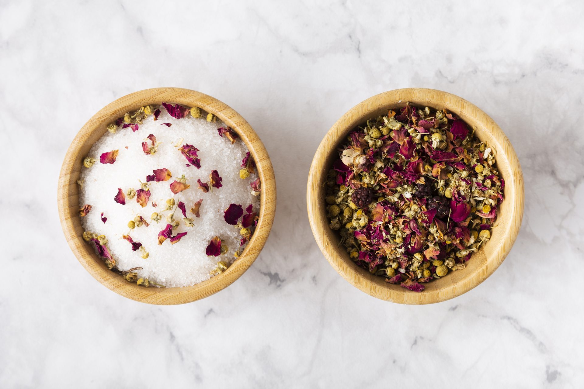 Two bamboo bowls on white marble, one of white salt with rose petals, one of dried flowers