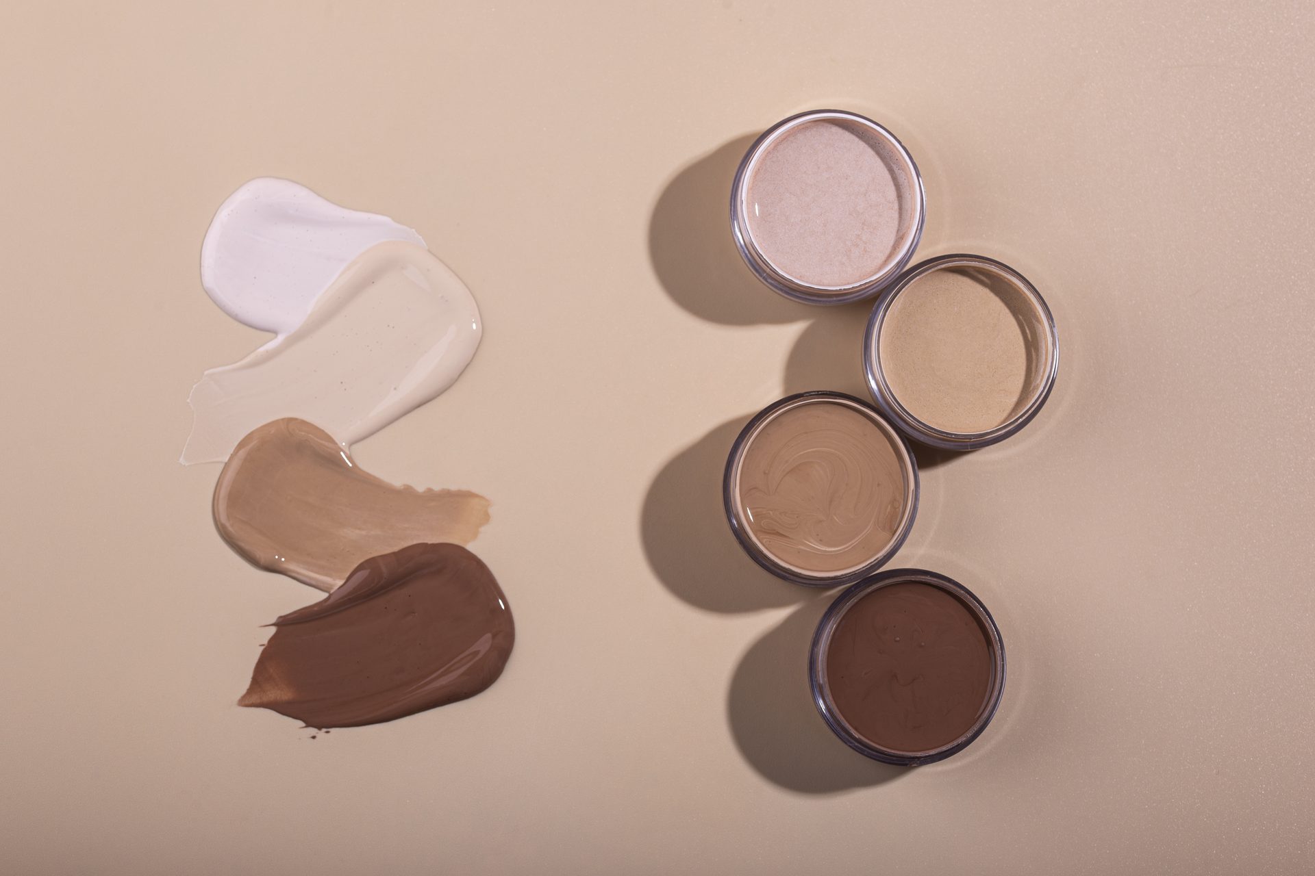Cream swatches from white to deep brown beside four open jars of matching shades on beige