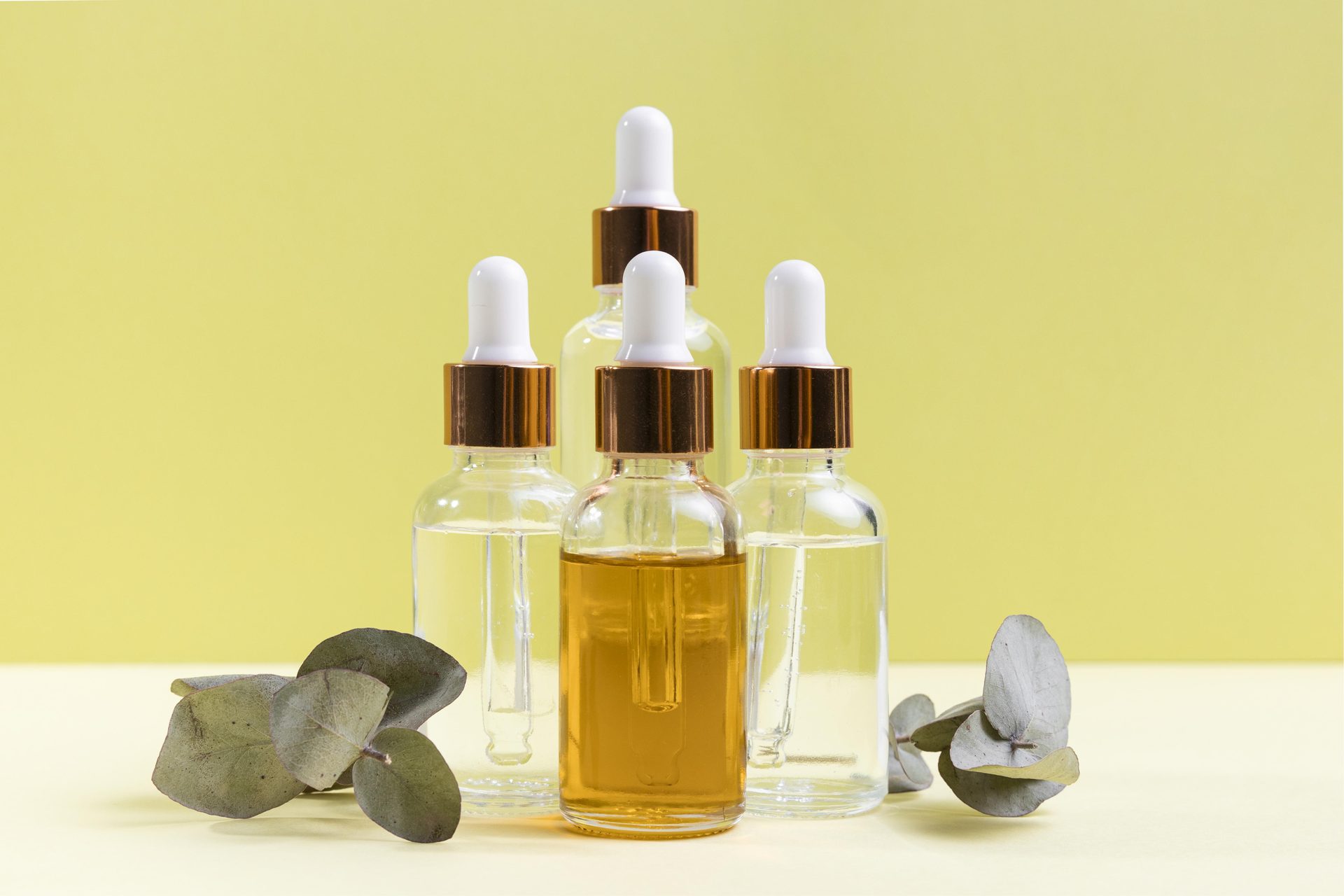 Cinco frascos cuentagotas de vidrio, uno con aceite ámbar, con hojas de eucalipto sobre fondo amarillo