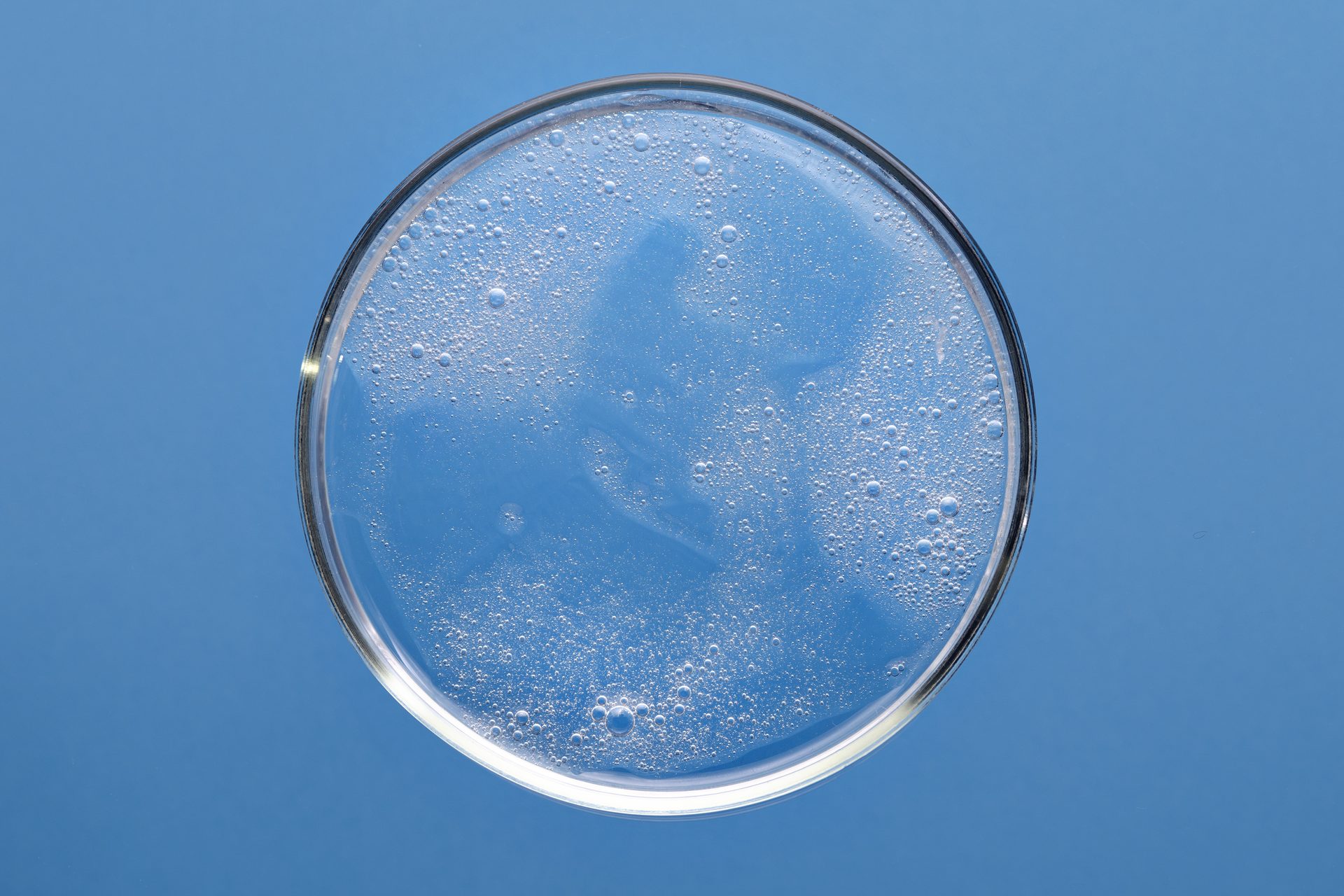Top view of a round glass dish of clear bubbly gel on a blue background