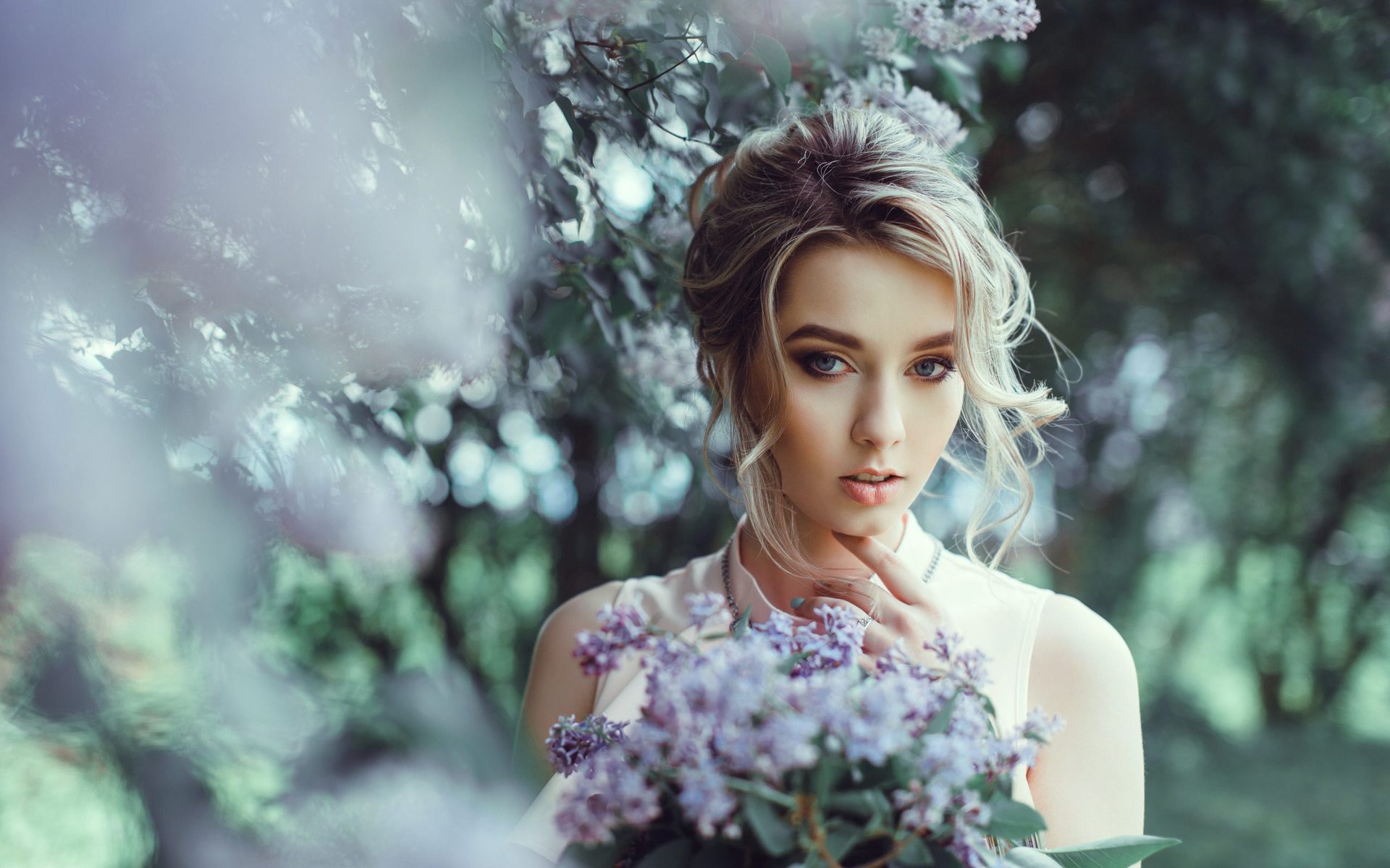 Young woman with an updo holding a bunch of lilac flowers among blossoming trees