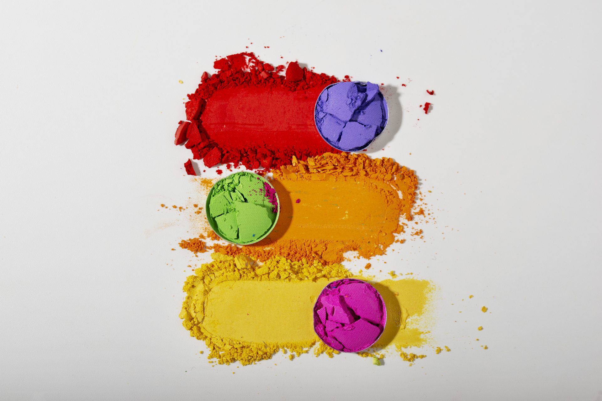 Crushed red, orange and yellow pigment swatches with purple, green and magenta pans on white