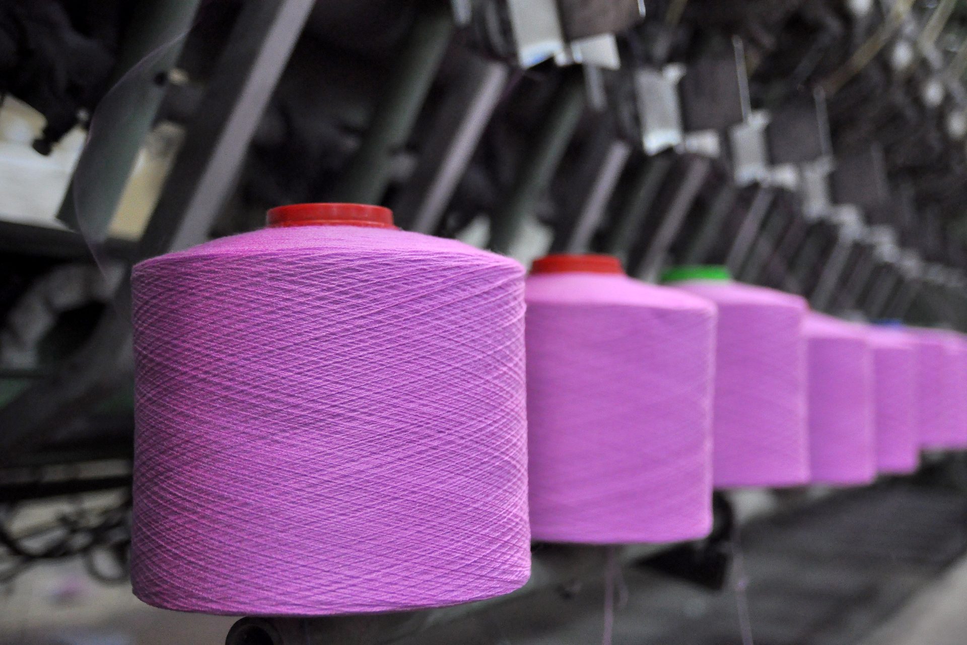 Hilera de grandes conos de hilo rosa montados en una máquina textil en una fábrica