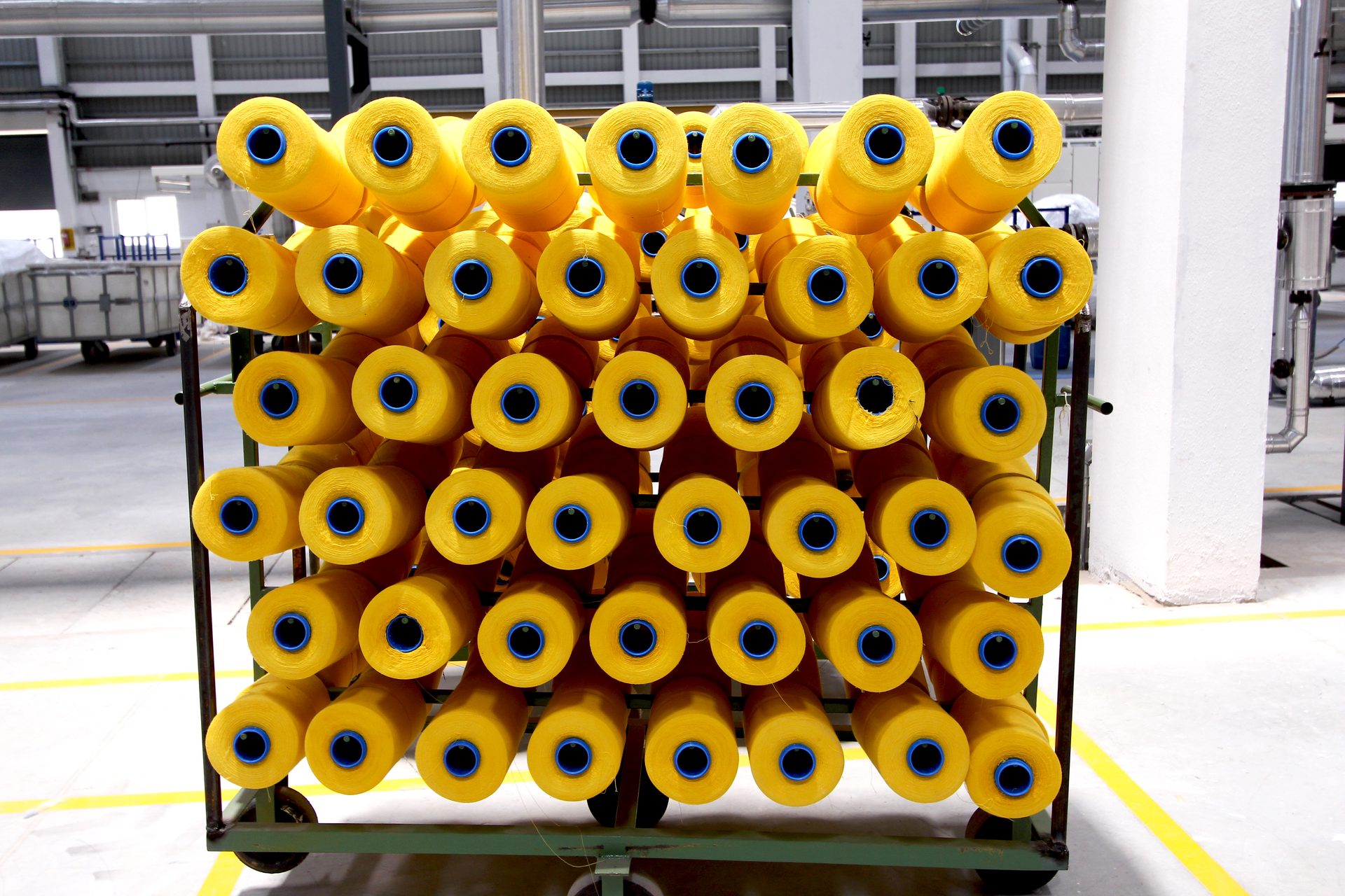 Metal trolley stacked with bright yellow yarn bobbins on a factory floor