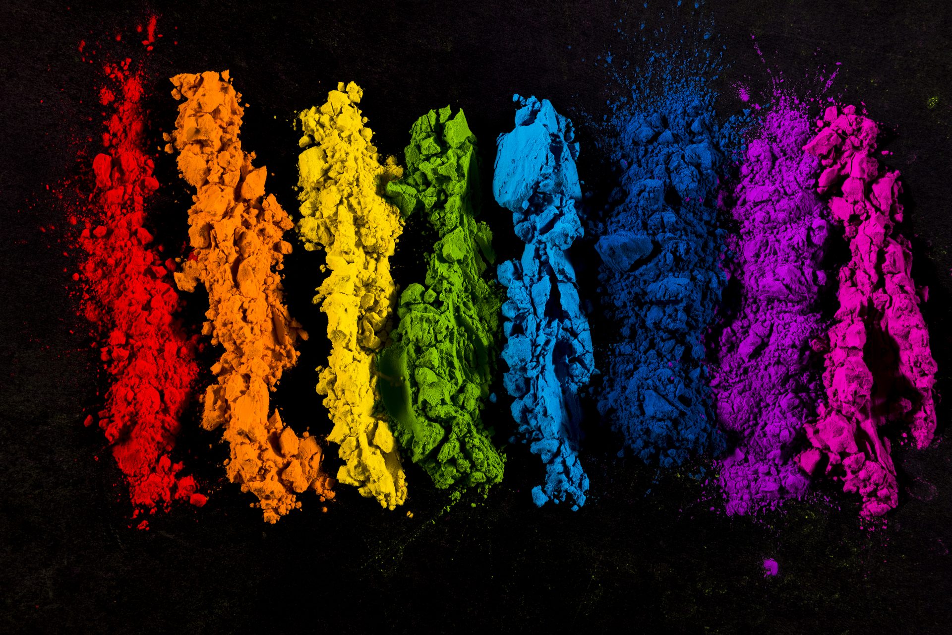 Stripes of powder pigment in rainbow order from red to magenta on a black background