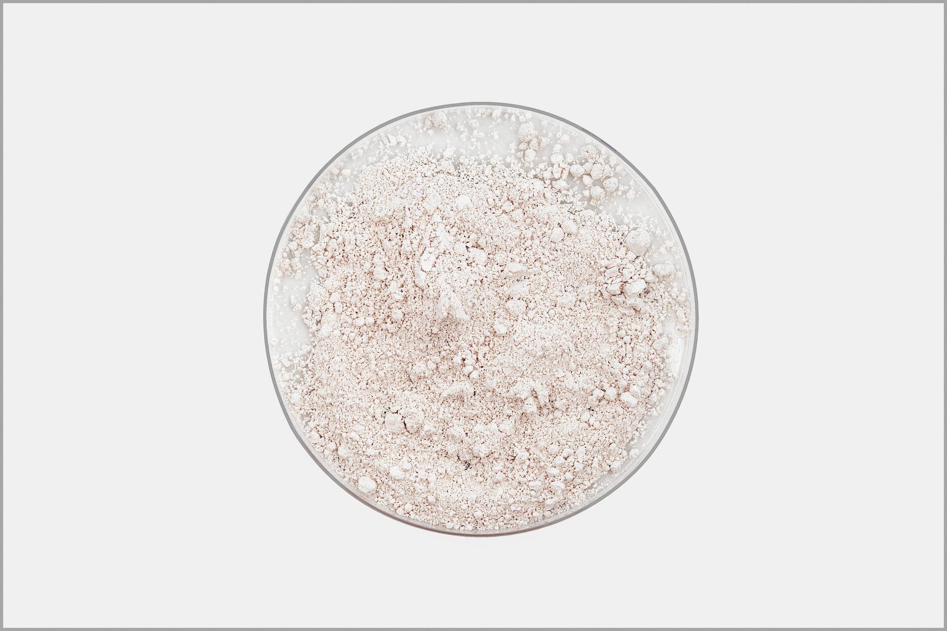 Vista cenital de polvo blanco rosado pálido en un recipiente redondo de vidrio sobre fondo gris claro