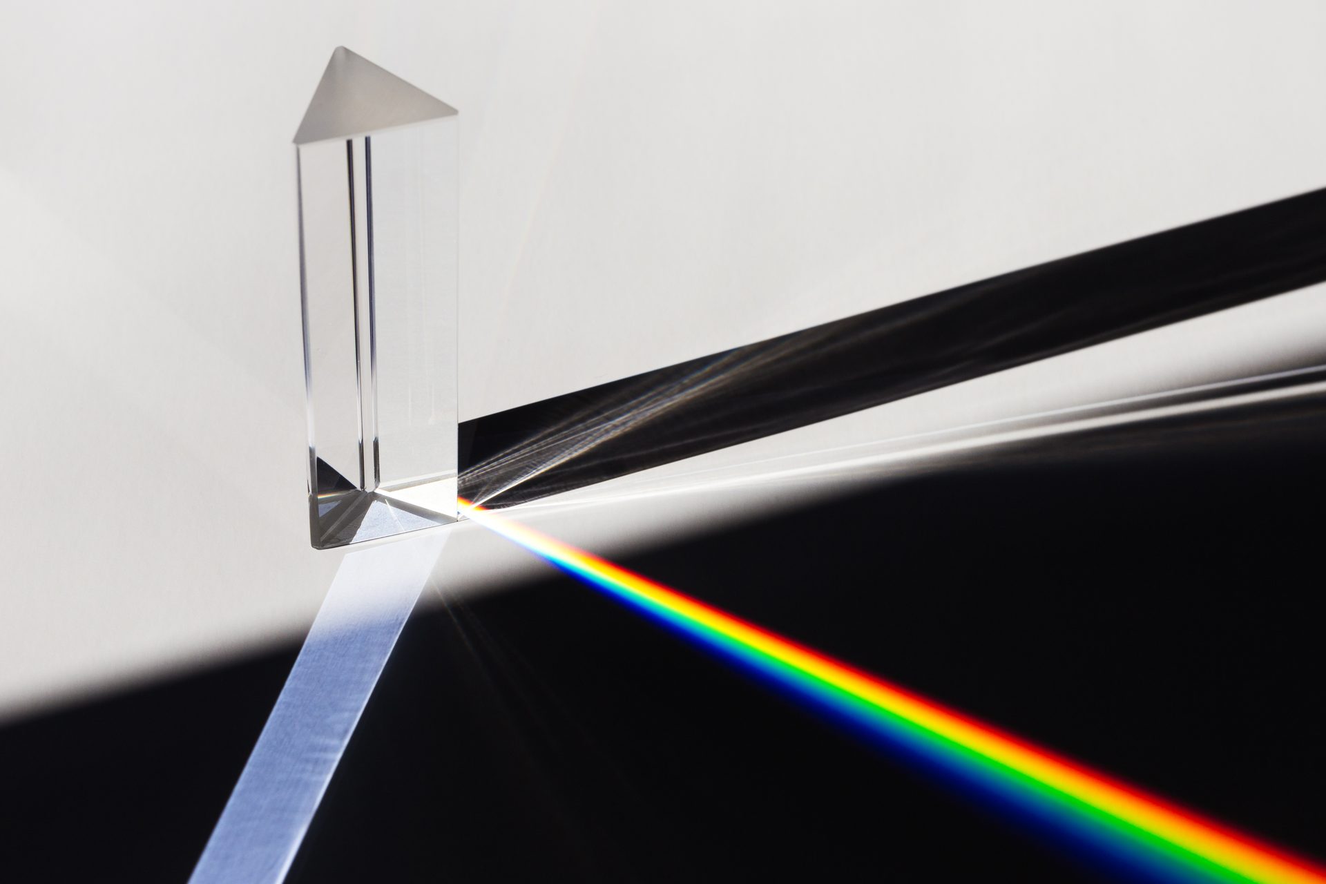 Glass prism splitting a beam of white light into a rainbow spectrum across a dark surface