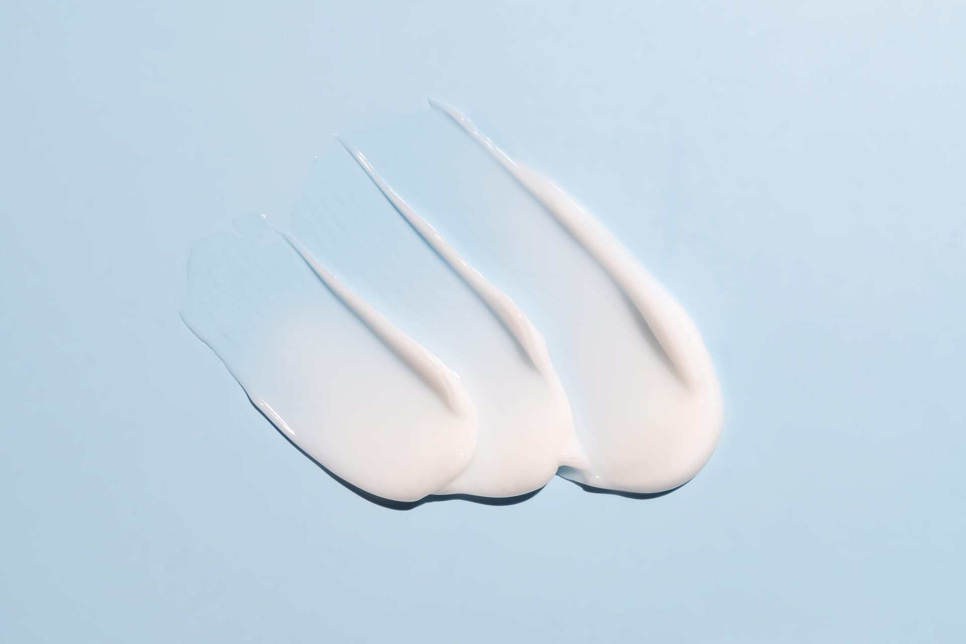 Tres muestras extendidas de crema blanca sobre un fondo azul claro