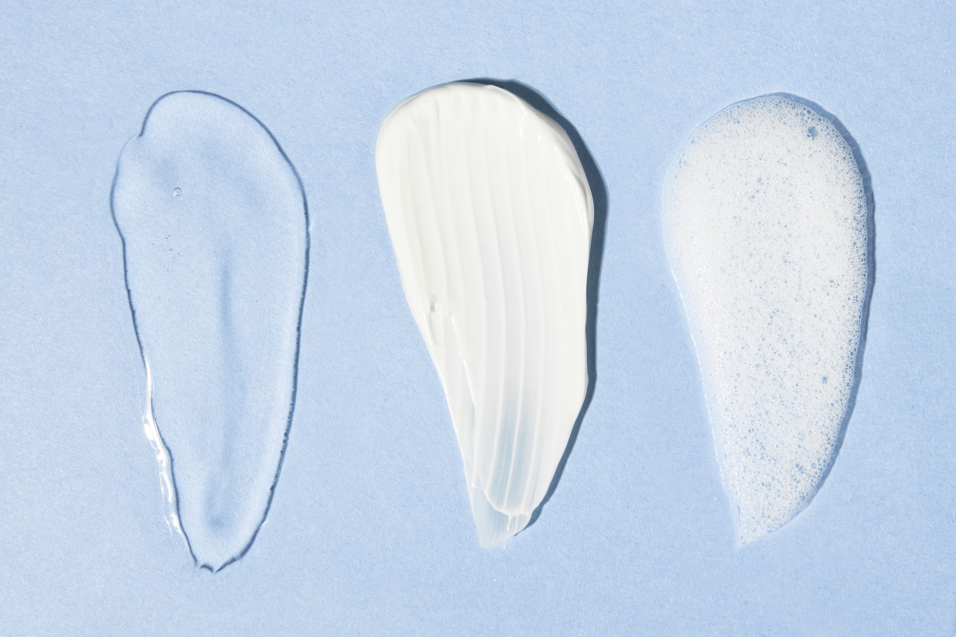 Tres muestras sobre azul claro: gel transparente, crema blanca y espuma blanca una junto a otra