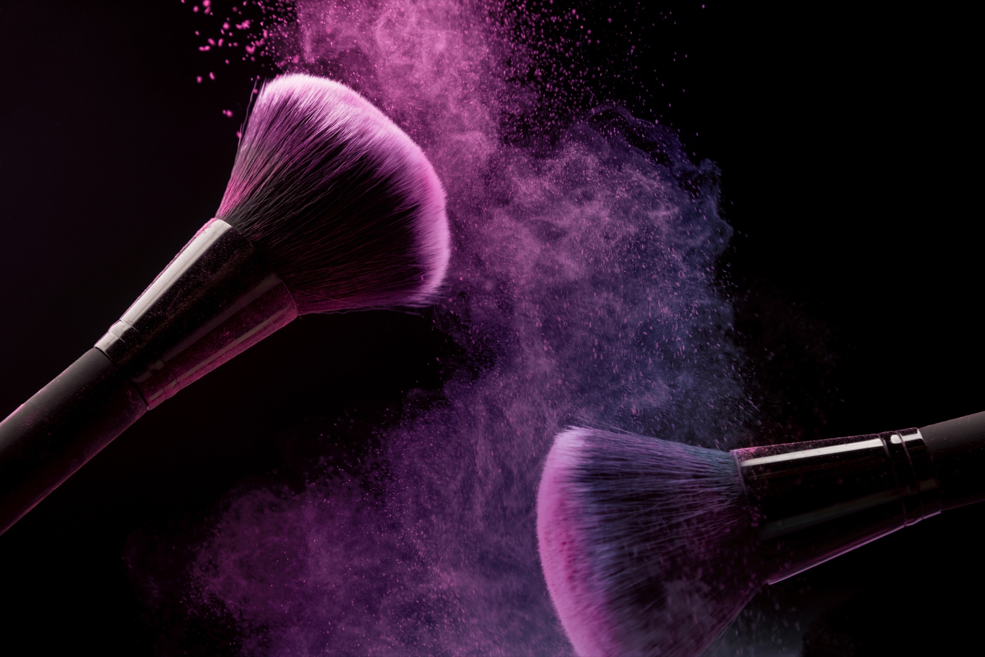 Two make-up brushes releasing clouds of violet powder against a black background