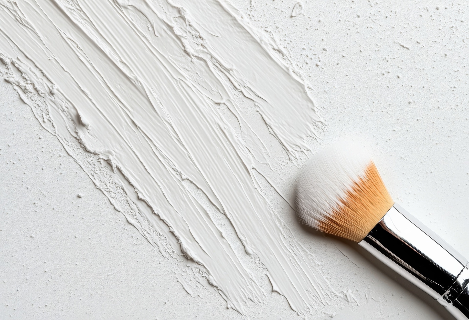 White brush strokes of thick cream on a white surface beside a make-up brush